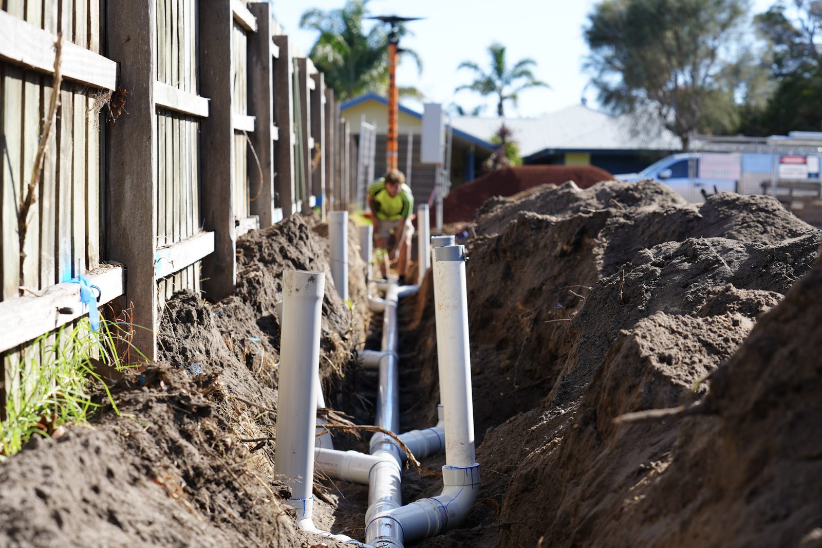 Row of white PVC stormwater risers standing in a trench along a fence line.
